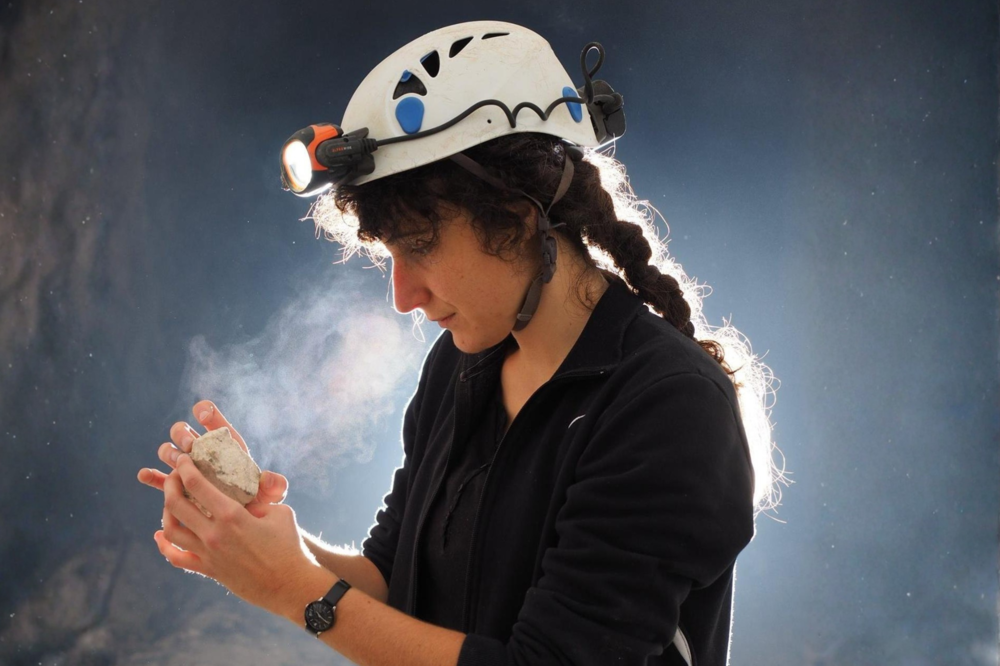 Veranstaltungsbild Céline Tomczyk untersucht mit Schutzhelm und Stirnlampe ein Gesteinsstück