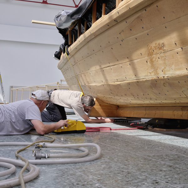 Facharbeiter liegen auf dem Boden neben dem Boot, um Luftkissen unter dem Nachbau anzubringen.