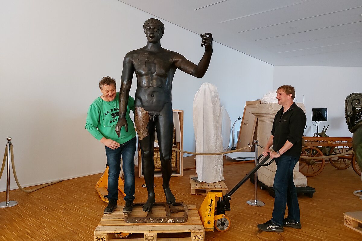 Zwei Mitarbeiter verschieben in der zukünftigen Ausstellung eine überlebensgroße Statue